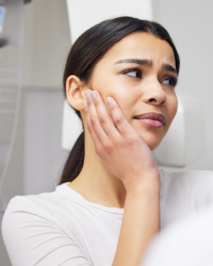 Woman holding her hand to her face in pain talking to dentist