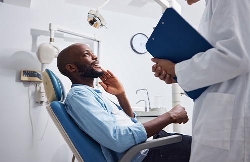 Man in blue shirt in dental chair smiling at dentist holding clipboard