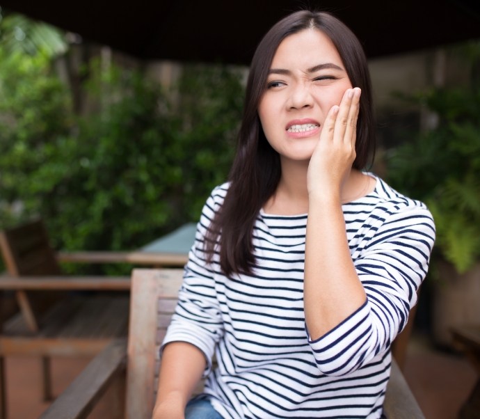 Woman wincing and holding her jaw needing emergency dentist in Braintree