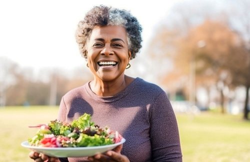 Woman smiling while holding plate of salad outside