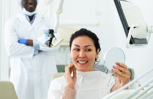 Happy dental patient holding hand mirror and smiling