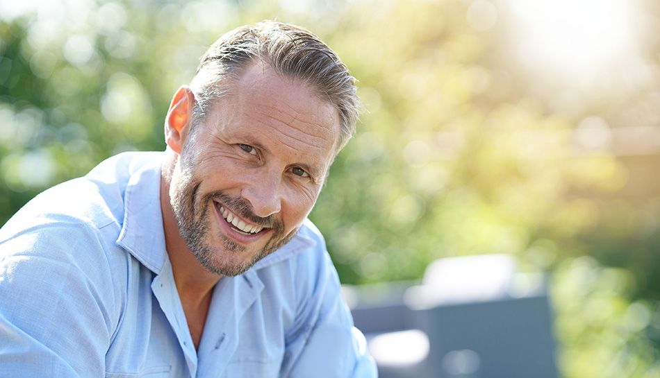 Smiling man outdoors in a light blue shirt with a blurred sunny background.