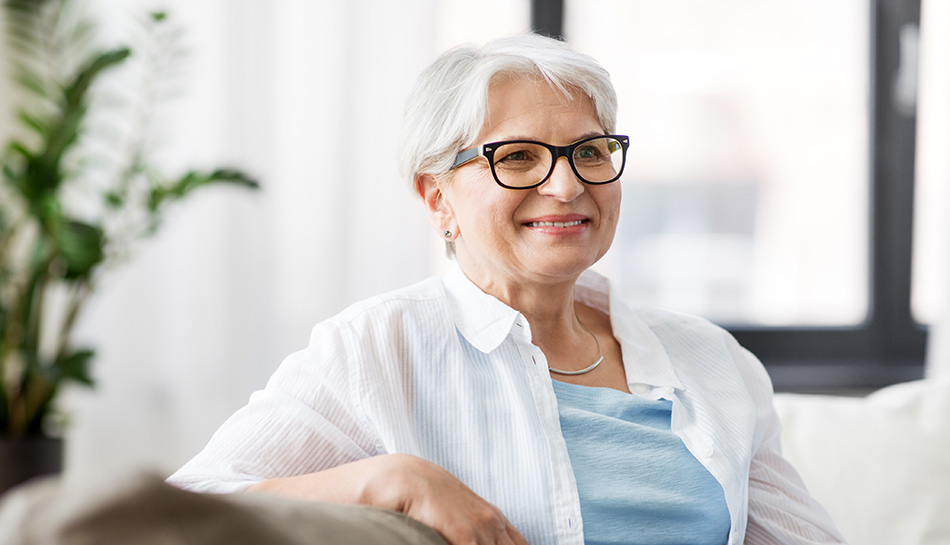 Older woman with white hair and glasses smiling while relaxing at home.