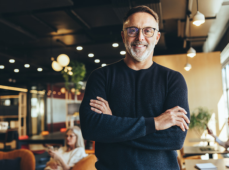 Smiling man with glasses standing confidently in a modern café or office space.