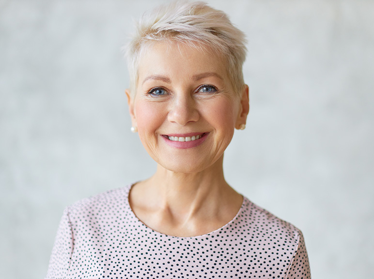 Portrait of a smiling older woman with short blonde hair against a light background.