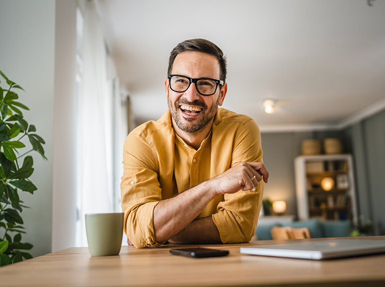 Smiling man with glasses leaning on a table in a cozy home office.