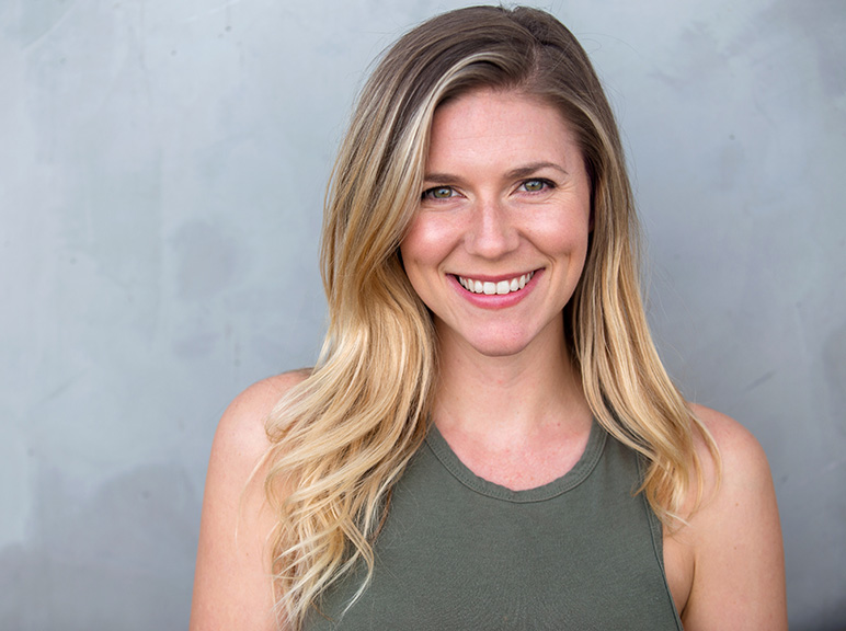Portrait of a smiling blonde woman in a sleeveless top against a gray background.