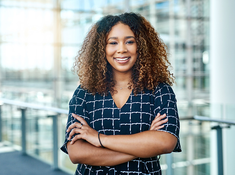 Smiling woman with curly hair standing confidently in a modern office building.