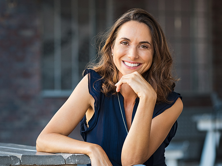 Woman smiling with hand resting on chin while sitting outdoors.