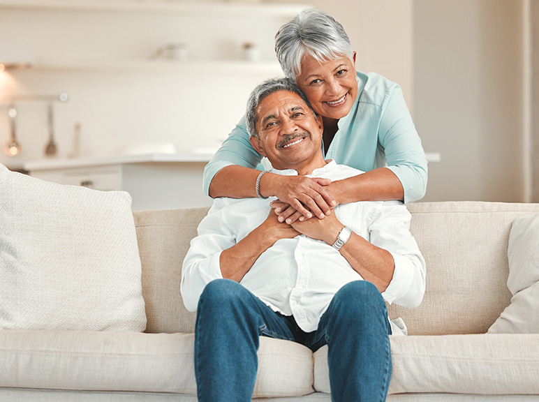 Older couple smiling and embracing while sitting together on a couch at home.