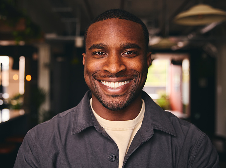 Close-up portrait of a smiling man in a dark jacket with a softly lit indoor background.