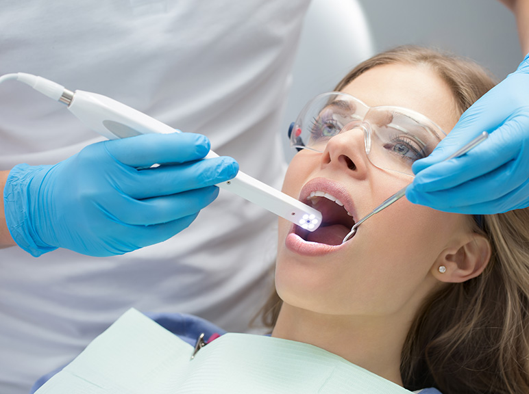 Dental professional examining a patient’s teeth with dental tools and protective eyewear.