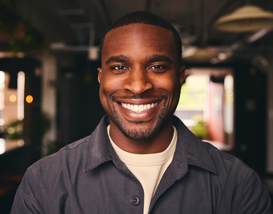 Close-up portrait of a smiling man in a dark jacket with a softly lit indoor background.