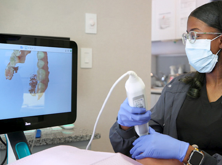 Dental professional using an intraoral scanner while reviewing 3D teeth images on a monitor.
